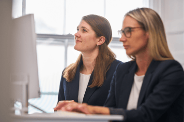 A photograph of two dental staff at a desk, one using a computer, the other smiling