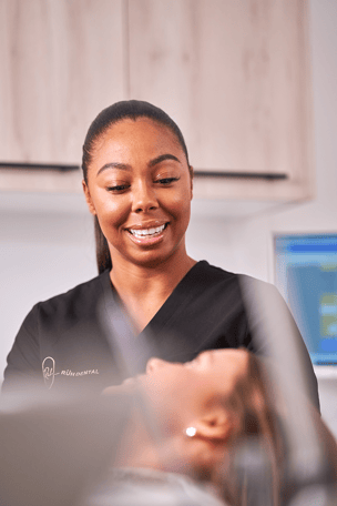 A photograph of a dentist smiling and looking at a patient laying in a dentist chair