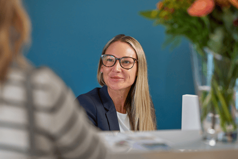 A photograph of a receptionist looking at and listening to a patient at the reception desk